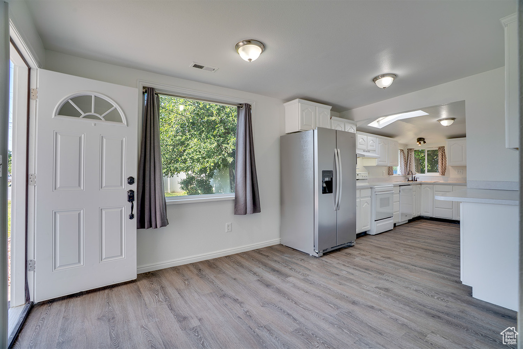 Kitchen with stainless steel fridge with ice dispenser, range, light countertops, under cabinet range hood, and light wood finished floors