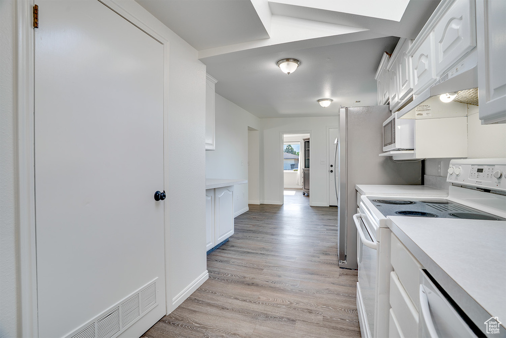 Kitchen featuring white appliances, white cabinets, light countertops, light wood-type flooring, and under cabinet range hood
