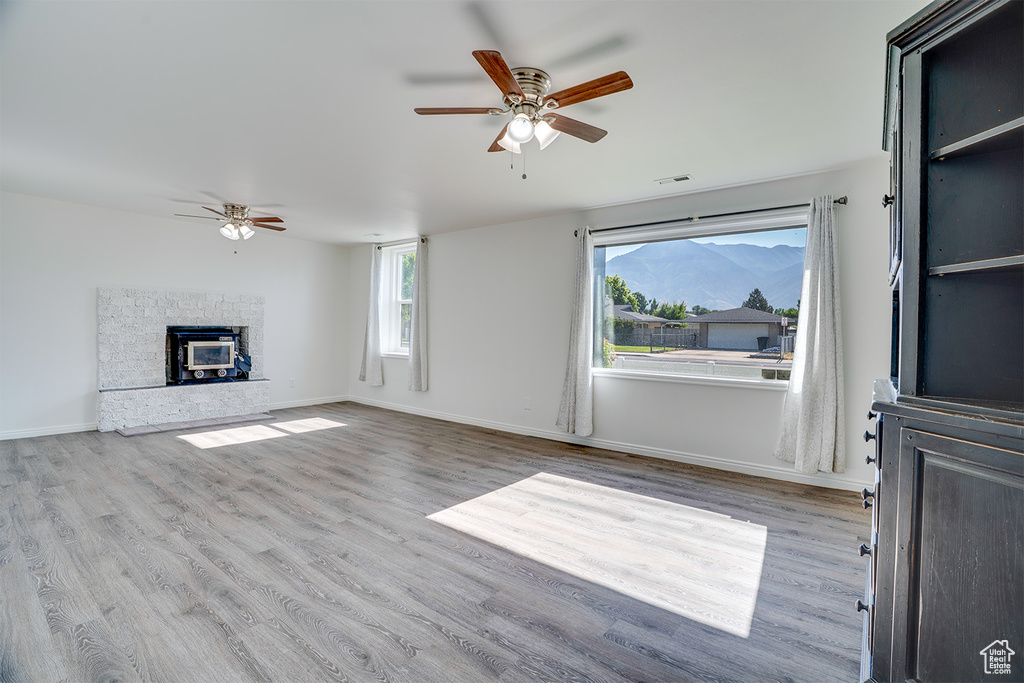 Unfurnished living room with ceiling fan, wood finished floors, and a glass covered fireplace