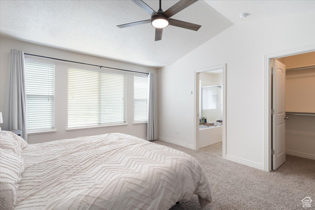 Bedroom featuring a spacious closet, lofted ceiling, light colored carpet, ensuite bathroom, and a ceiling fan