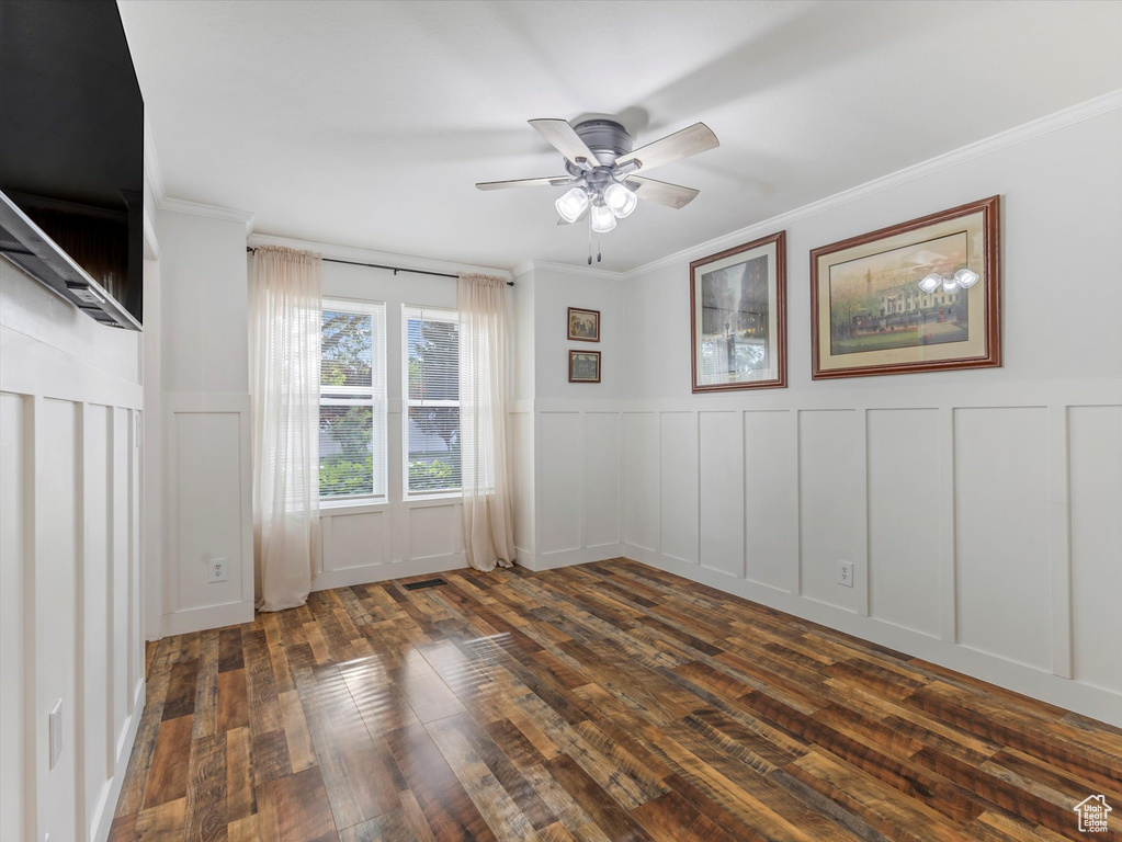 Unfurnished room with a decorative wall, dark wood-style floors, ceiling fan, crown molding, and wainscoting