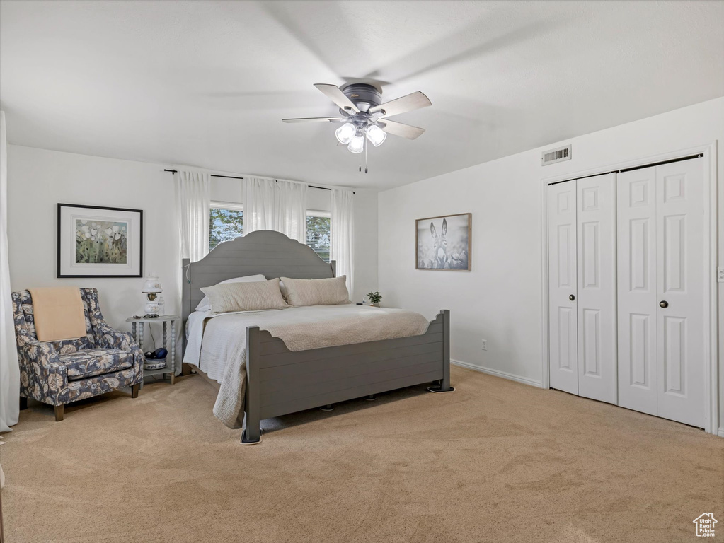 Bedroom featuring light colored carpet, a ceiling fan, and a closet