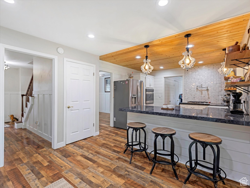 Kitchen with appliances with stainless steel finishes, dark wood-style floors, a breakfast bar area, white cabinetry, and decorative light fixtures