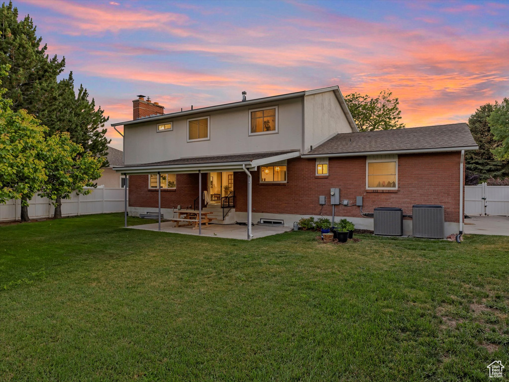 Back of property at dusk featuring a patio, a chimney, a fenced backyard, brick siding, and roof with shingles