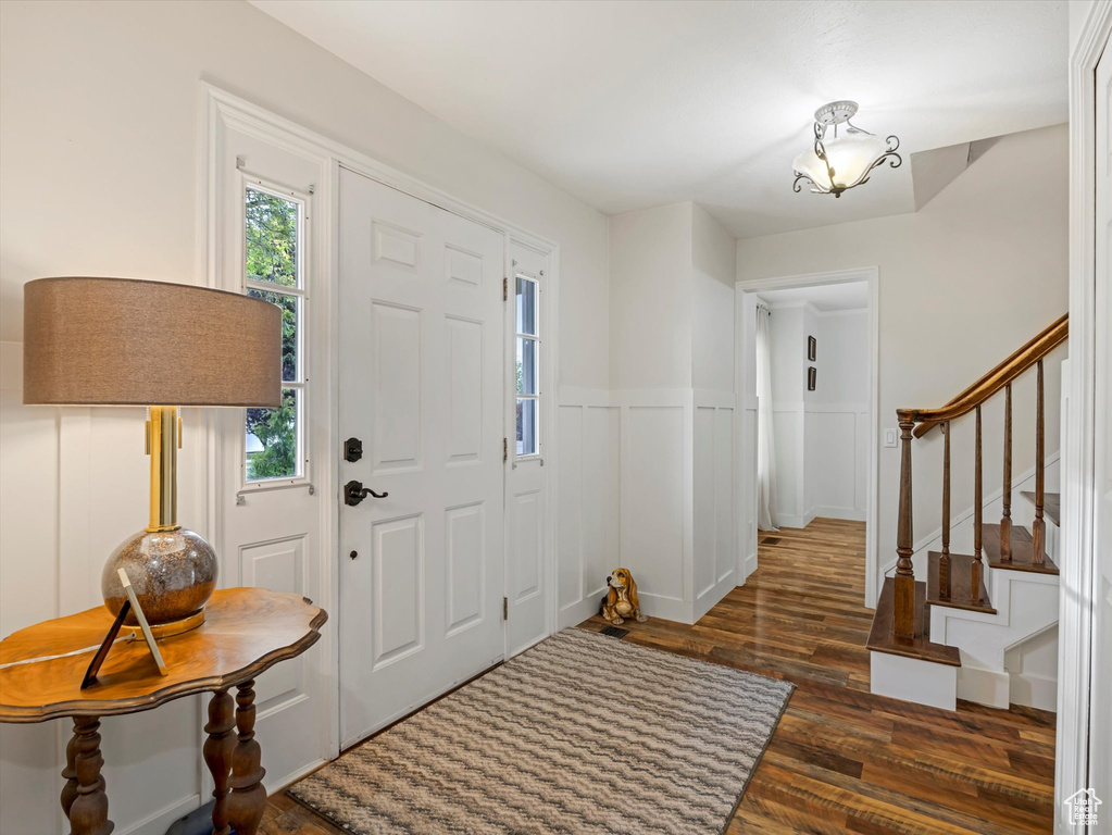 Foyer entrance with dark wood-style flooring, stairs, and a wainscoted wall