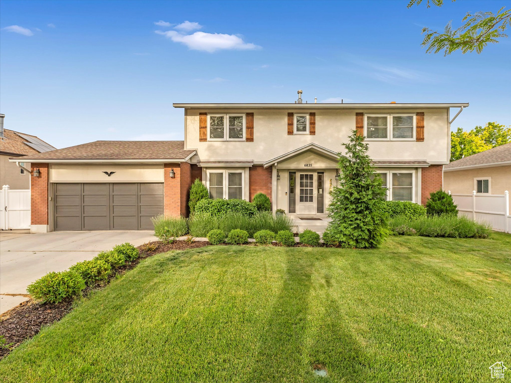 Traditional-style home featuring an attached garage, driveway, brick siding, and stucco siding