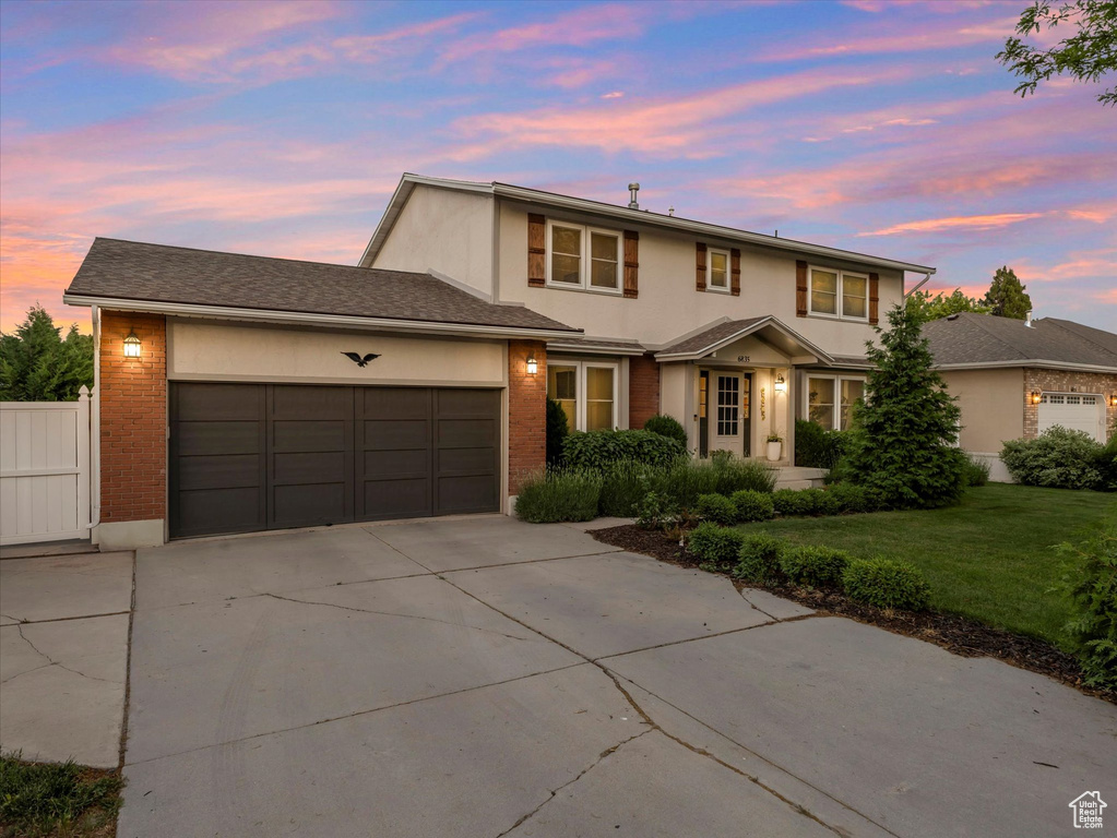 Traditional-style home featuring driveway, a garage, a yard, and brick siding