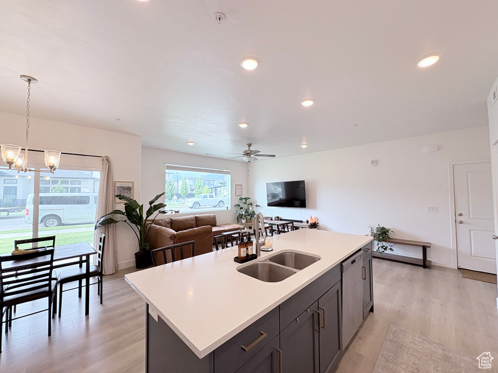Kitchen featuring light wood-type flooring, open floor plan, light countertops, stainless steel dishwasher, and a chandelier