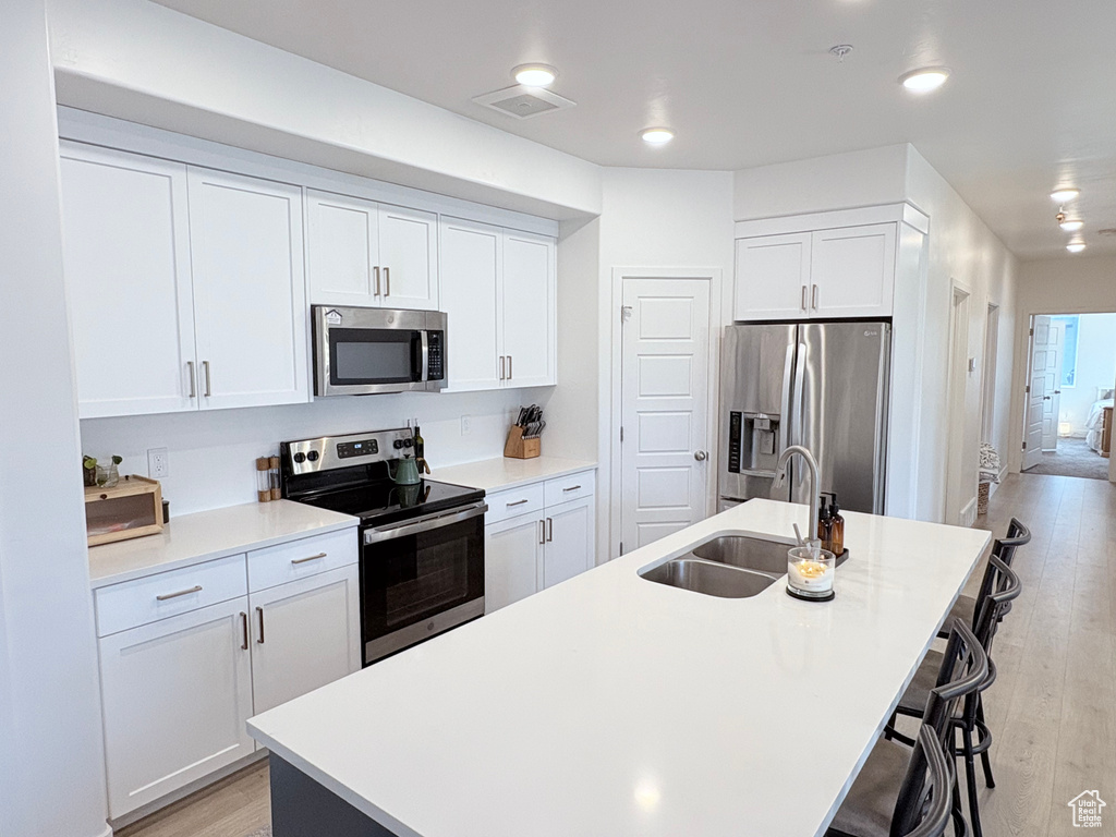 Kitchen featuring appliances with stainless steel finishes, an island with sink, a breakfast bar, light wood-style flooring, and white cabinetry