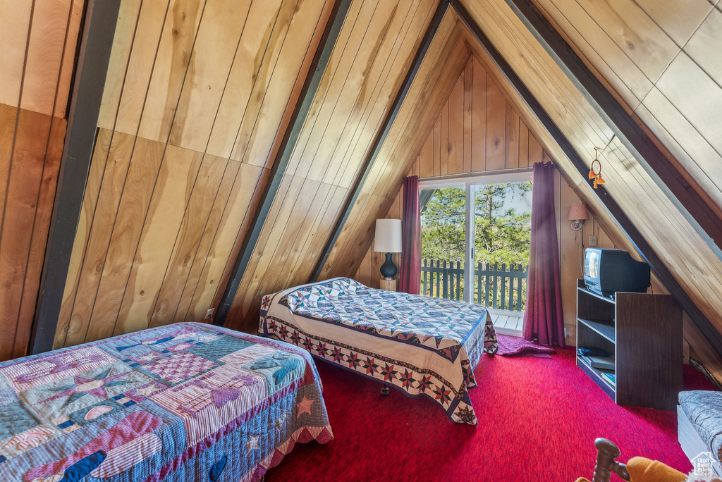 Carpeted bedroom featuring lofted ceiling, wood walls, and access to outside