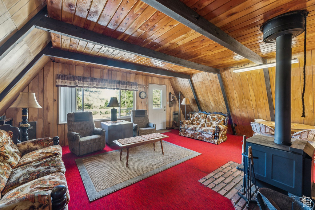 Carpeted living room with a wood stove, wood walls, and a wooden ceiling with exposed beams