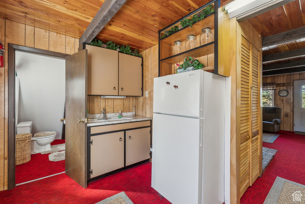 Kitchen featuring freestanding refrigerator, a wood ceiling with exposed beams, carpet, light countertops, and wooden walls