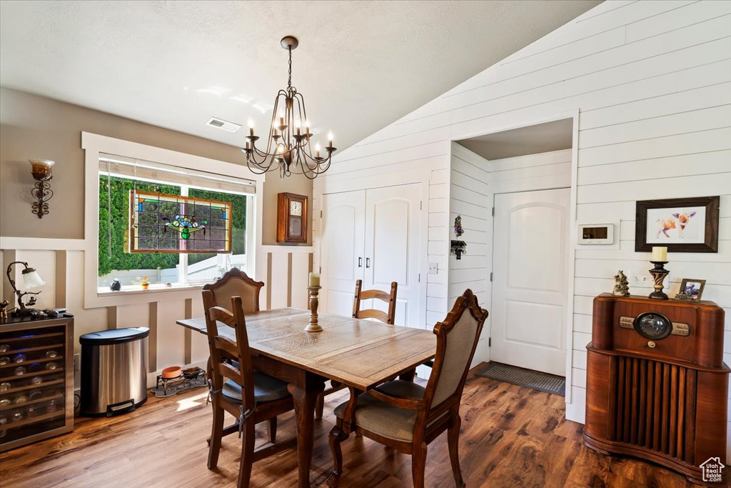 Dining area featuring vaulted ceiling, a chandelier, wood finished floors, wood walls, and wine cooler