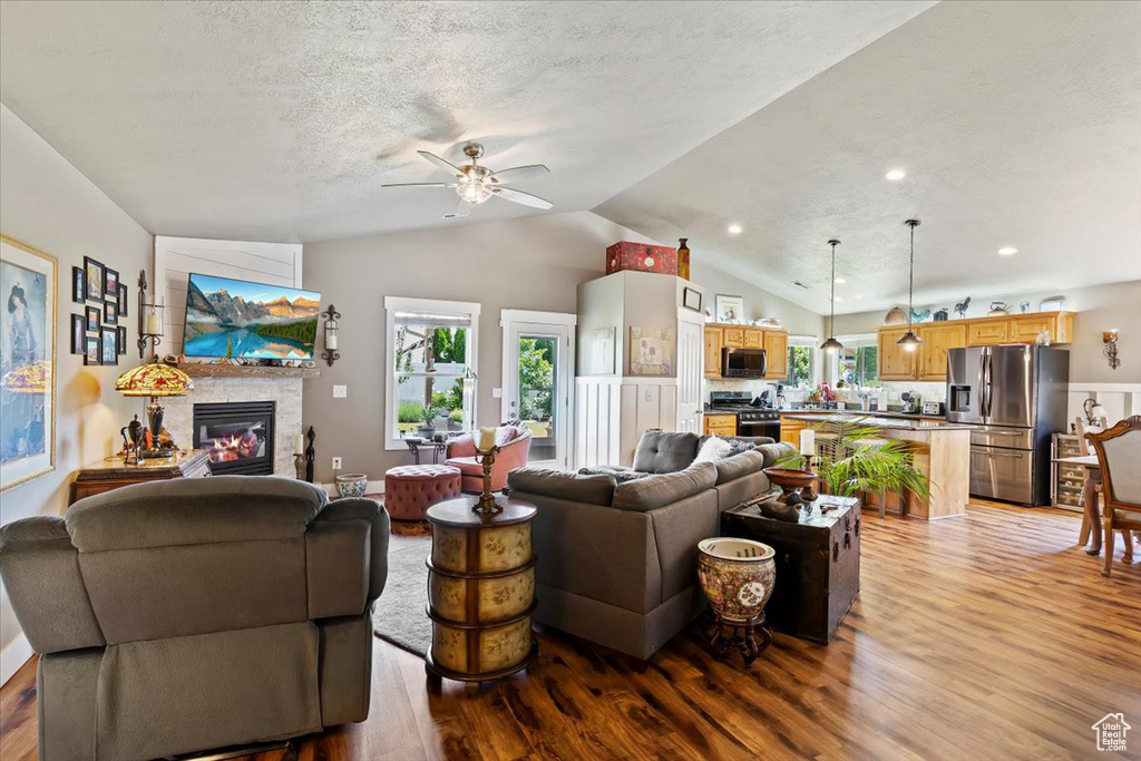 Living room featuring light wood-style flooring, a ceiling fan, lofted ceiling, a glass covered fireplace, and a textured ceiling