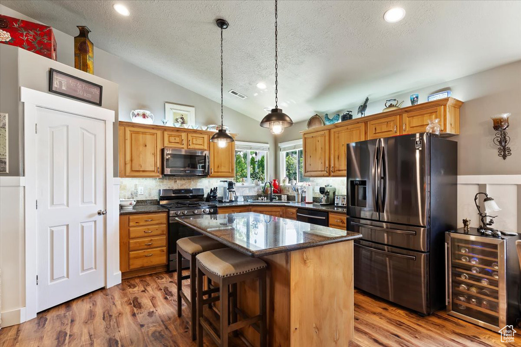 Kitchen featuring stainless steel appliances, beverage cooler, a textured ceiling, vaulted ceiling, and tasteful backsplash