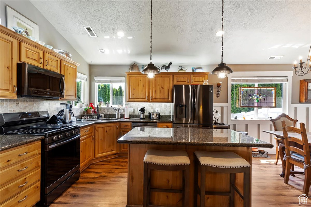 Kitchen with range with gas stovetop, black microwave, stainless steel fridge with ice dispenser, a textured ceiling, and wood finished floors