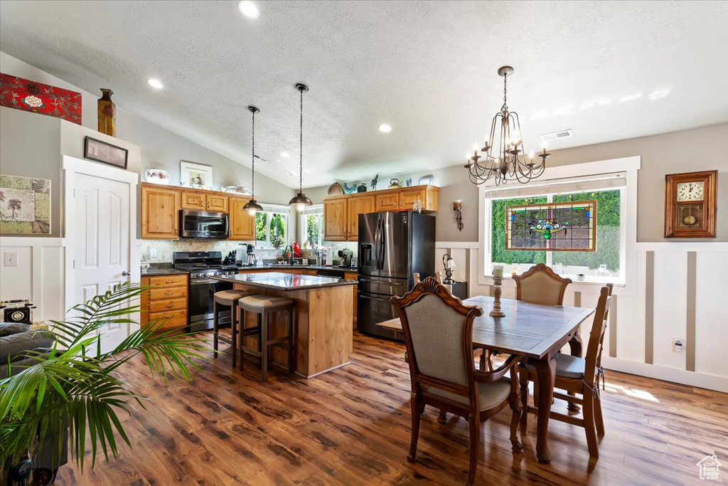 Kitchen featuring stainless steel appliances, dark wood-style floors, a decorative wall, vaulted ceiling, and a chandelier