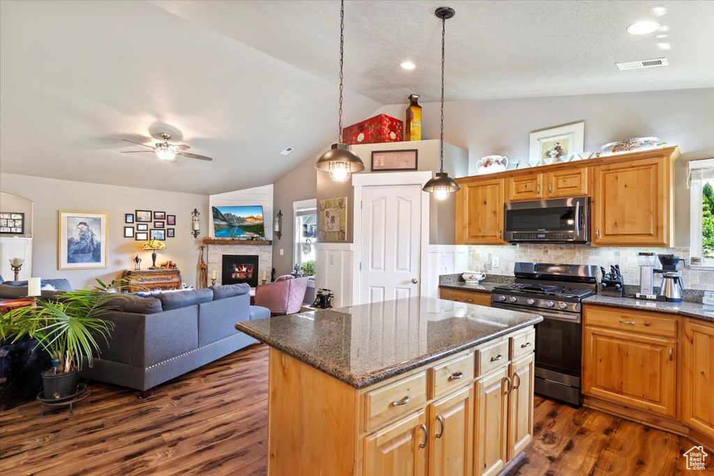 Kitchen featuring appliances with stainless steel finishes, vaulted ceiling, dark wood-type flooring, ceiling fan, and a kitchen island