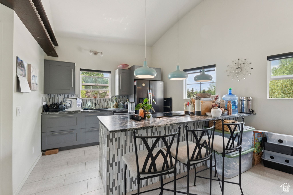 Kitchen featuring stainless steel refrigerator with ice dispenser, gray cabinetry, healthy amount of natural light, and high vaulted ceiling