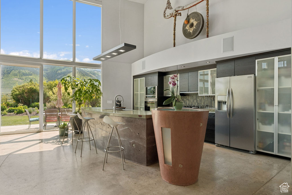Kitchen with stainless steel appliances, a towering ceiling, backsplash, a sink, and a breakfast bar