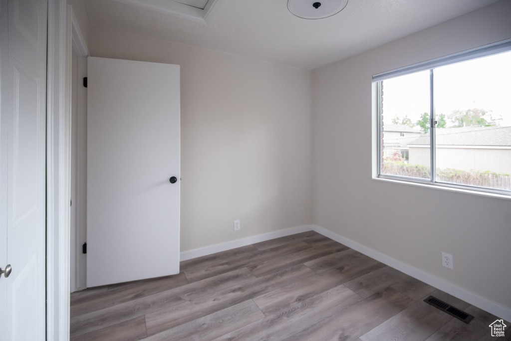 Unfurnished room with wood finished floors, baseboards, and attic access
