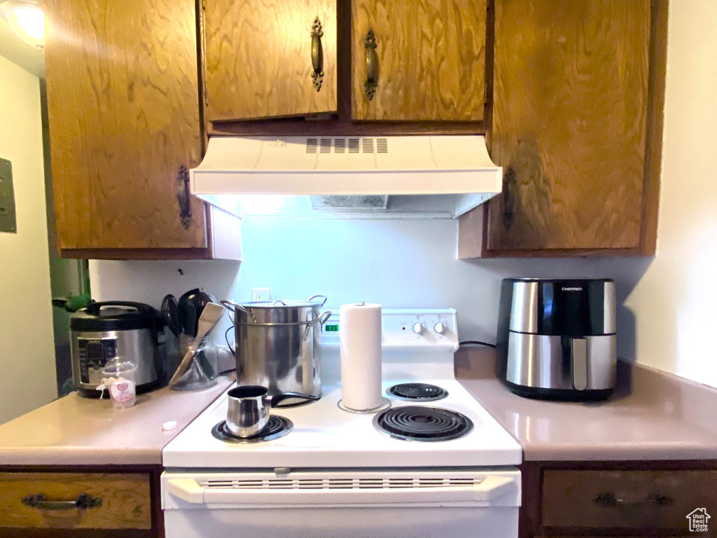 Kitchen featuring under cabinet range hood, white electric stove, light countertops, and brown cabinets