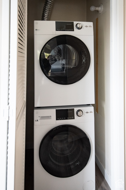 Laundry room featuring stacked washer and clothes dryer, wood finished floors, and baseboards