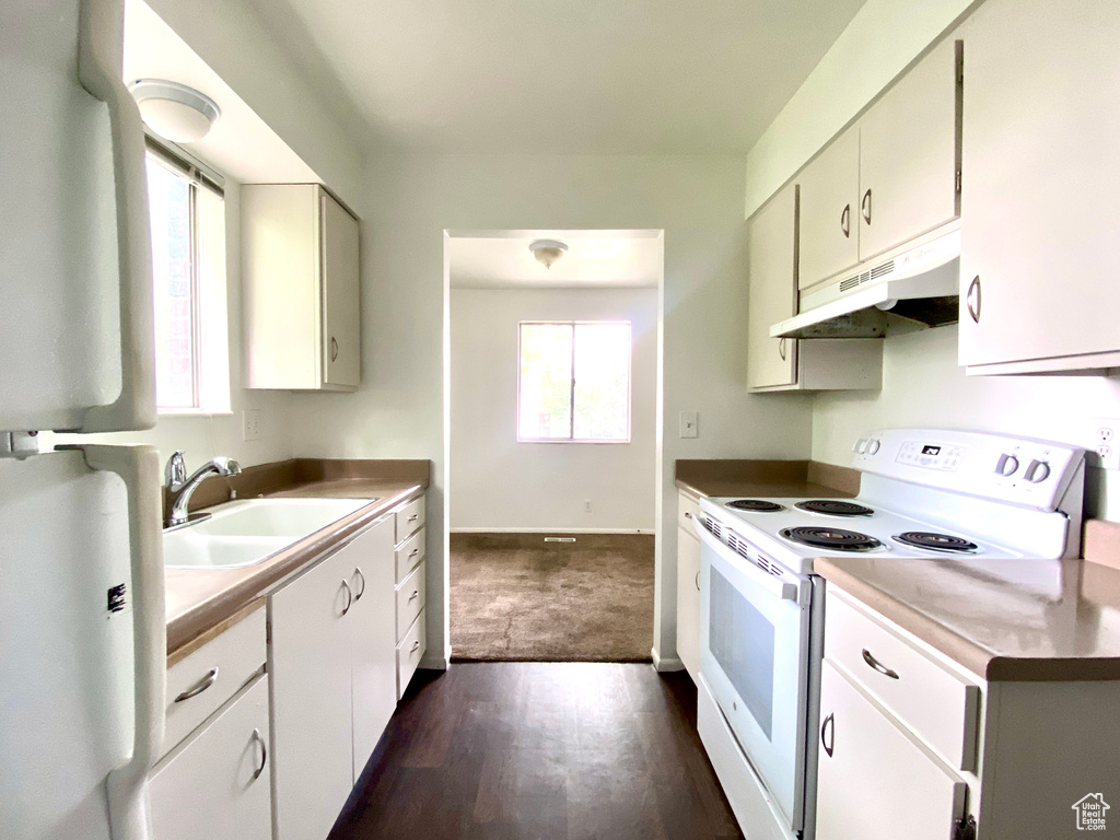 Kitchen featuring white electric stove, under cabinet range hood, a sink, dark wood-style floors, and baseboards