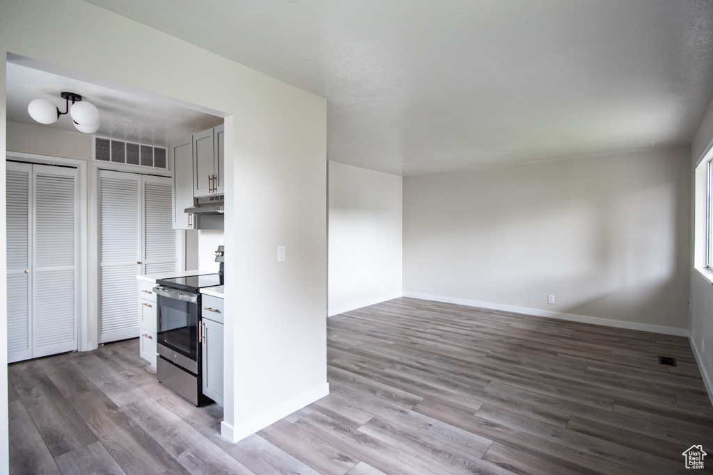 Kitchen with electric range, under cabinet range hood, light wood-type flooring, light countertops, and baseboards