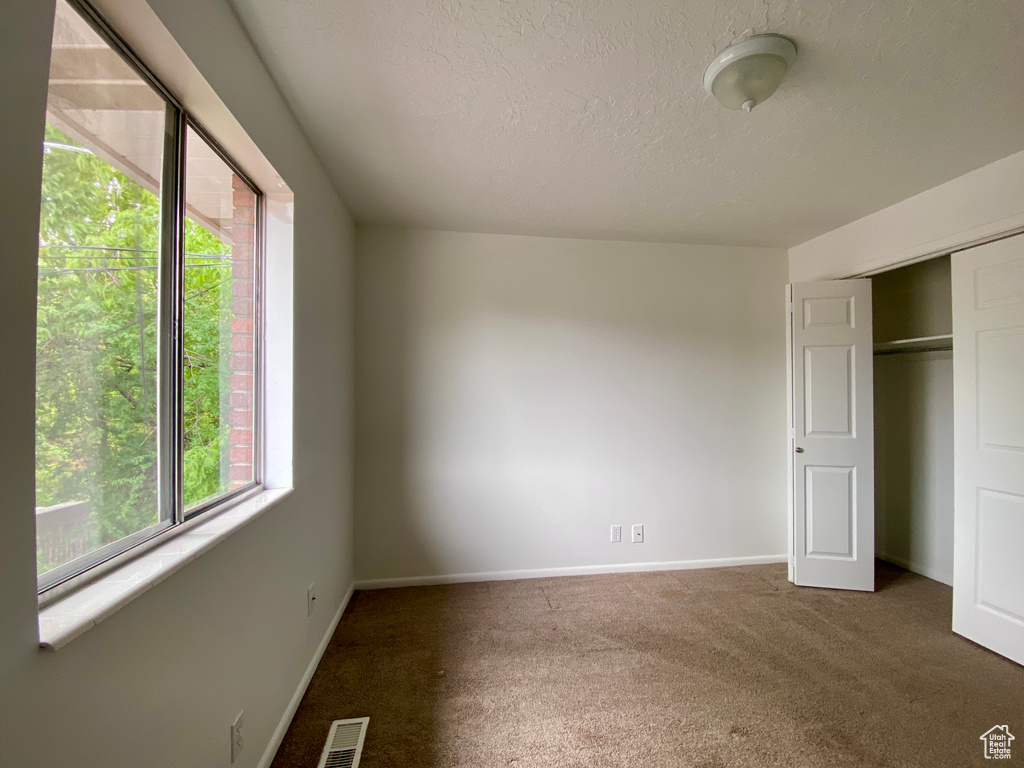 Unfurnished bedroom featuring carpet, baseboards, a textured ceiling, and a closet