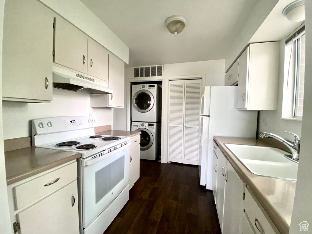 Kitchen with white appliances, under cabinet range hood, stacked washer / dryer, a sink, and dark wood-type flooring
