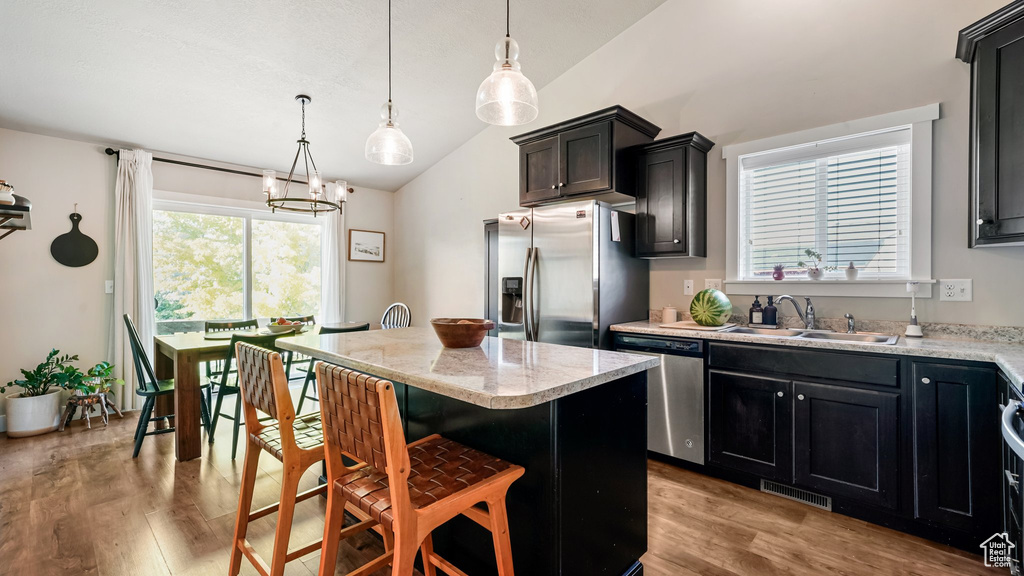 Kitchen with appliances with stainless steel finishes, vaulted ceiling, a sink, light wood-style flooring, and a kitchen island