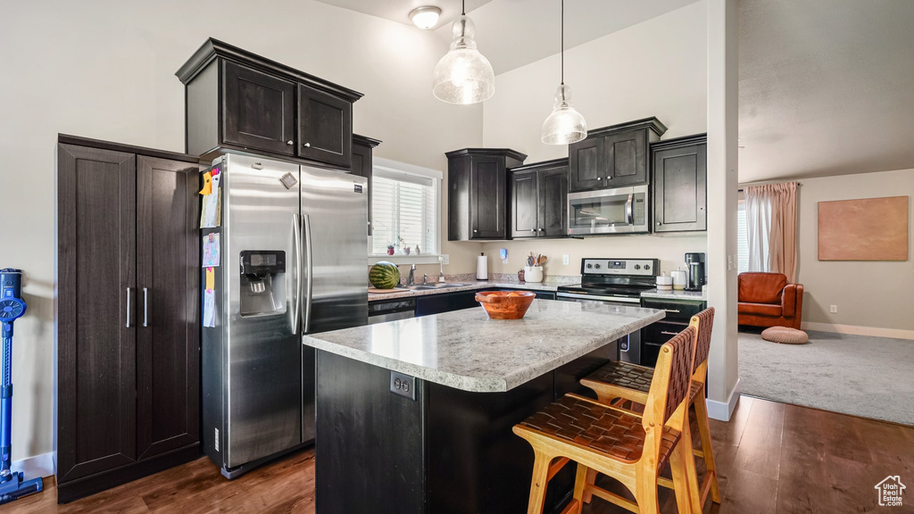 Kitchen with stainless steel appliances, a kitchen island, a breakfast bar, baseboards, and decorative light fixtures