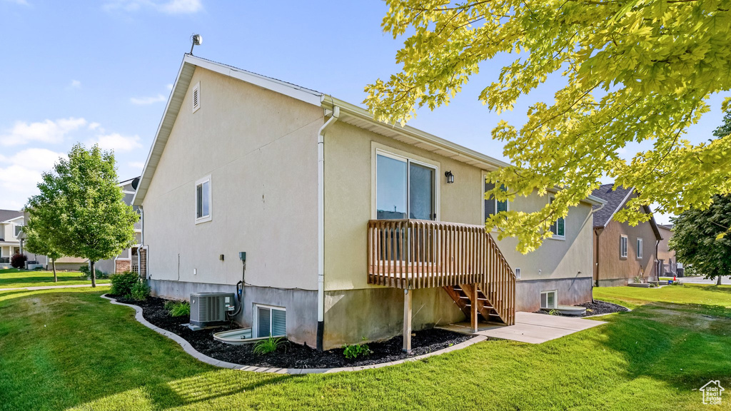 Back of property with a lawn, stucco siding, and central air condition unit