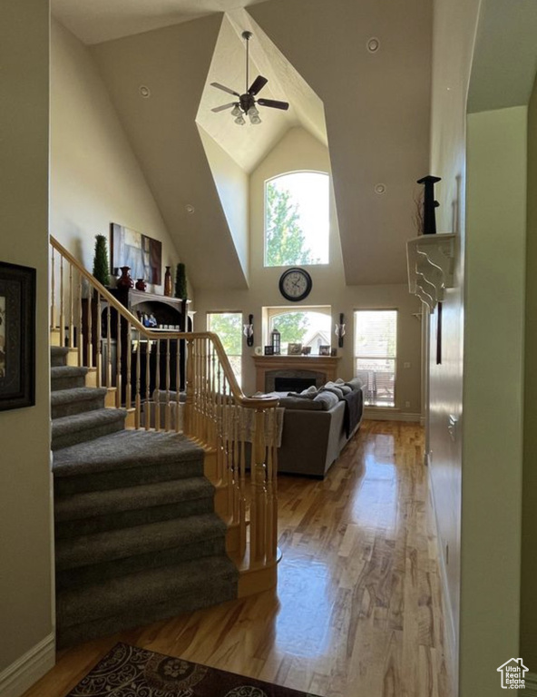Stairs with plenty of natural light, wood finished floors, high vaulted ceiling, and ceiling fan