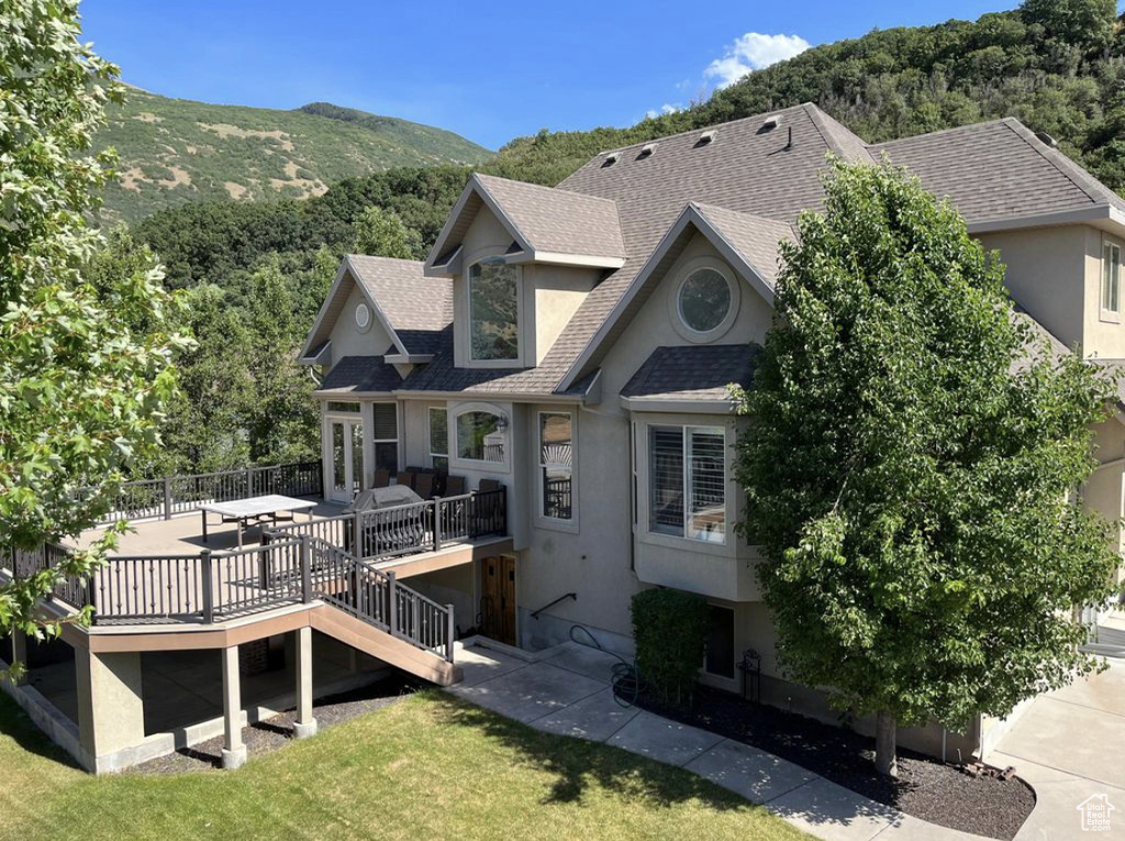 Rear view of house with a shingled roof, stucco siding, a deck with mountain view, and a yard