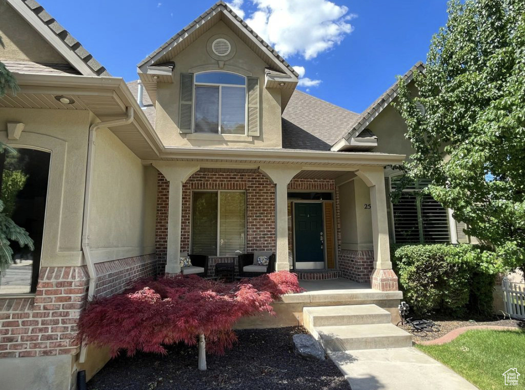 View of exterior entry with covered porch, brick siding, and stucco siding