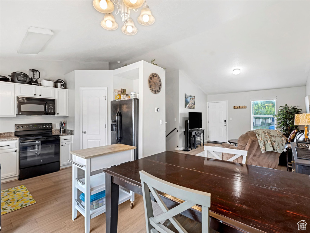 Kitchen with black appliances, white cabinets, lofted ceiling, open floor plan, and light wood finished floors