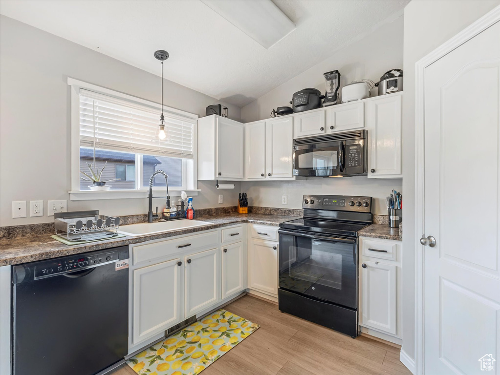 Kitchen featuring black appliances, white cabinets, light wood-type flooring, vaulted ceiling, and hanging light fixtures