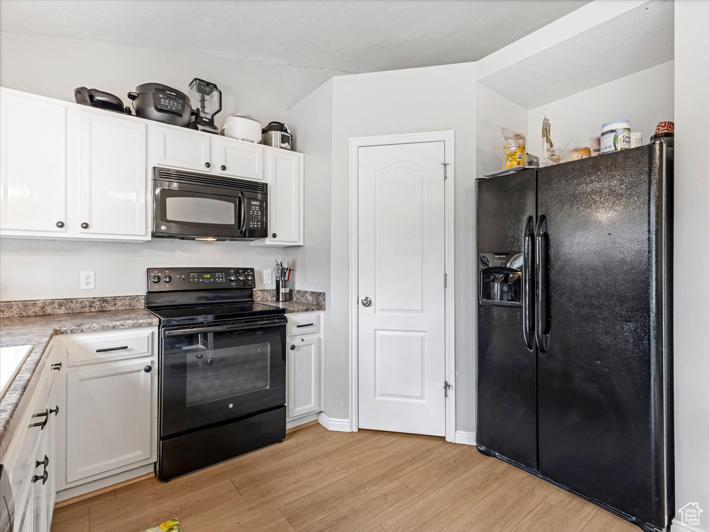 Kitchen featuring black appliances, light wood-type flooring, white cabinets, and light countertops