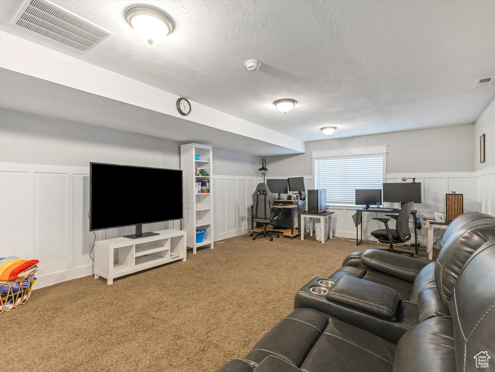 Living room featuring a decorative wall, an office area, carpet flooring, a textured ceiling, and wainscoting
