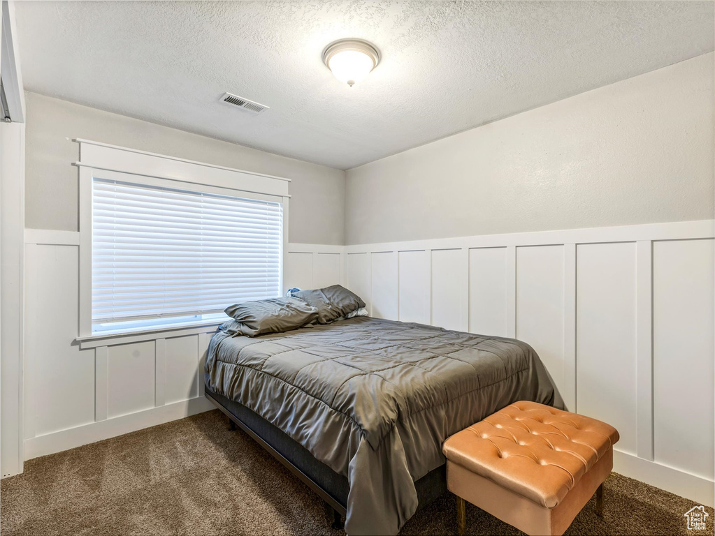 Carpeted bedroom with a textured ceiling, a decorative wall, and wainscoting