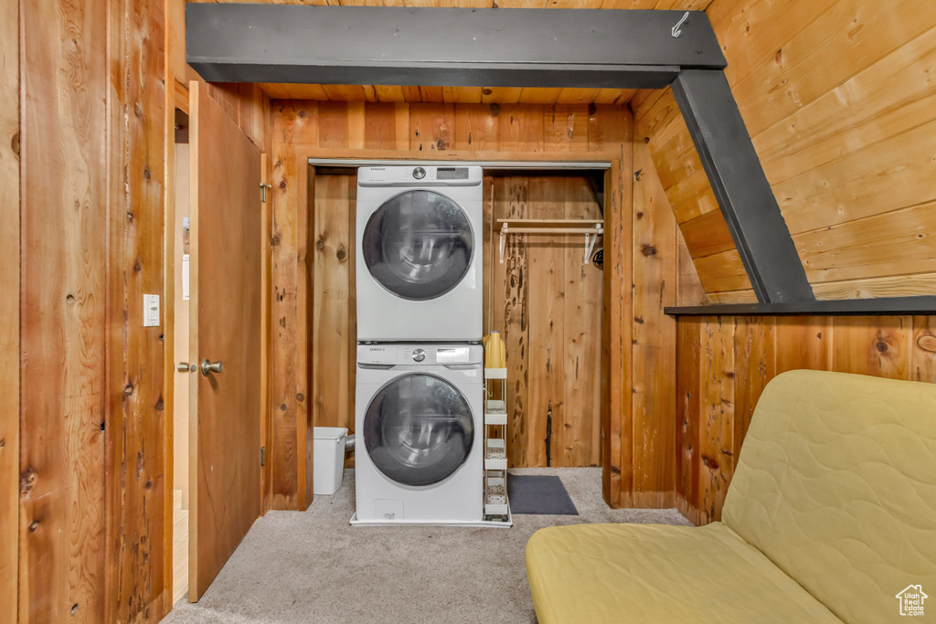 Laundry area featuring stacked washer / drying machine, carpet, and wooden walls