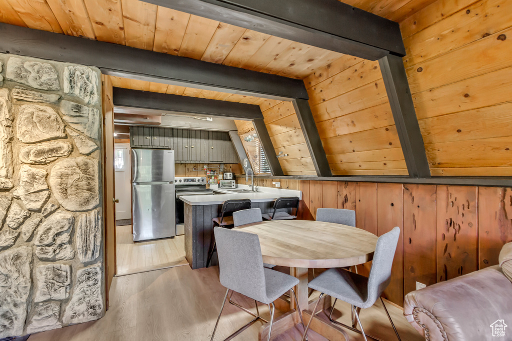 Dining space with wooden walls, a wooden ceiling with exposed beams, and light wood-type flooring