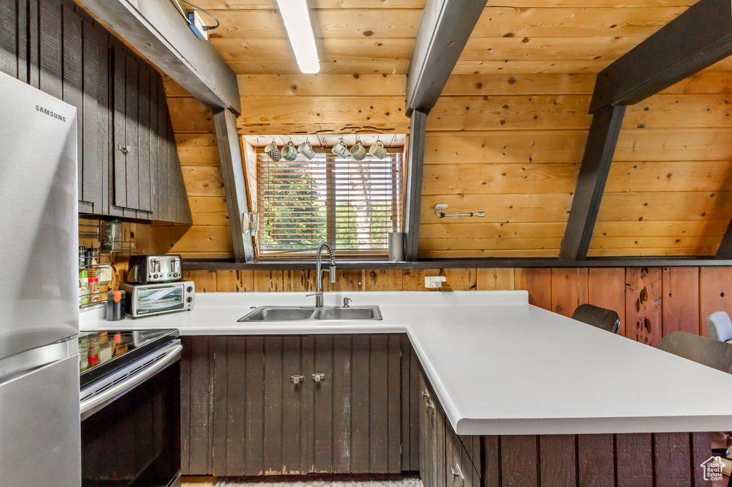 Kitchen featuring stainless steel appliances, light countertops, a wooden ceiling with exposed beams, and wood walls