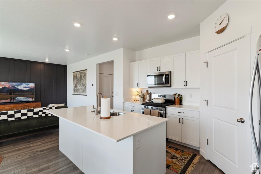 Kitchen with stainless steel appliances, an island with sink, white cabinets, light countertops, and recessed lighting