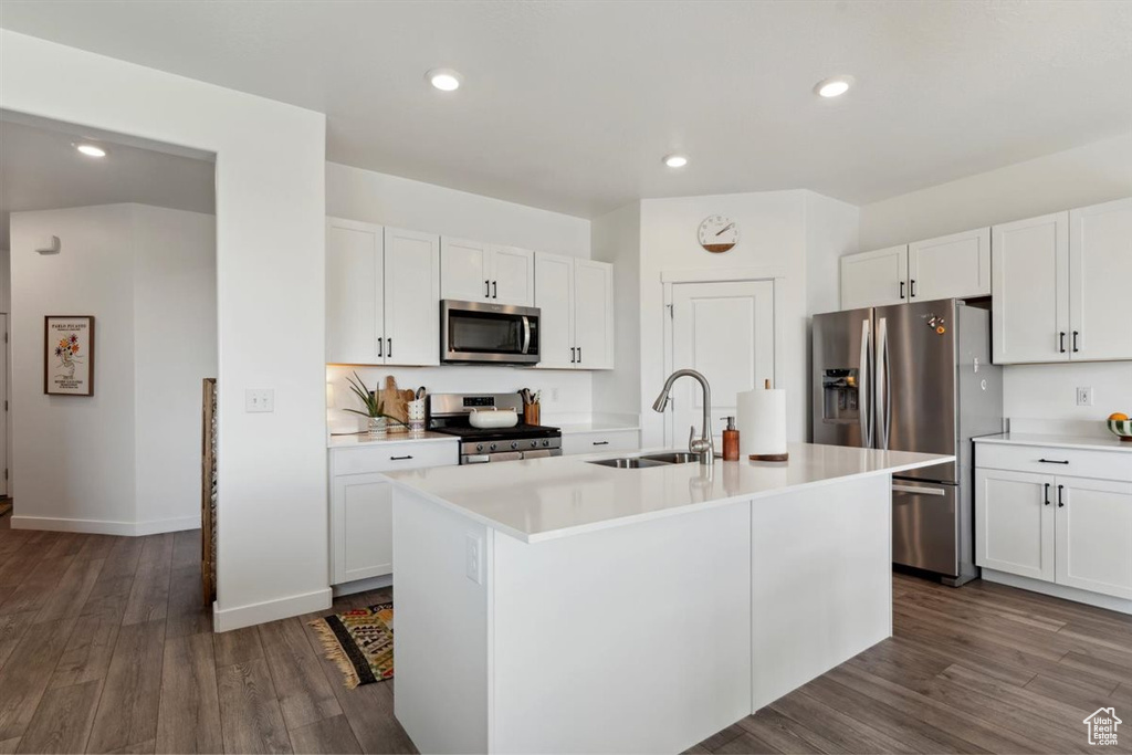 Kitchen with stainless steel appliances, an island with sink, light countertops, white cabinetry, and dark wood finished floors