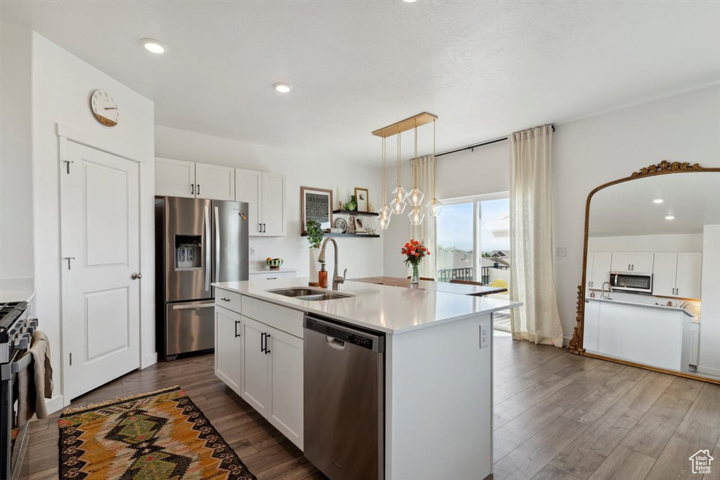 Kitchen featuring appliances with stainless steel finishes, dark wood-style flooring, white cabinets, light countertops, and a kitchen island with sink