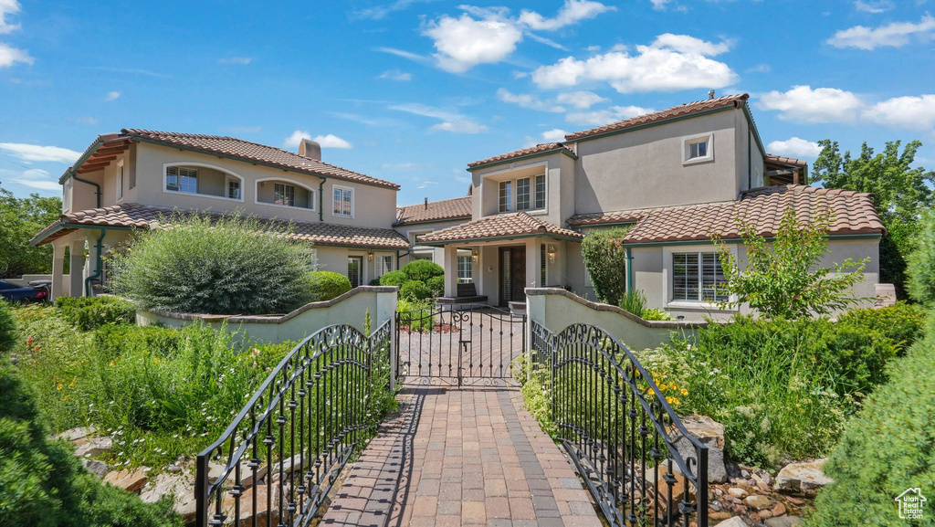 Mediterranean / spanish-style house with a fenced front yard, a tiled roof, stucco siding, and a gate