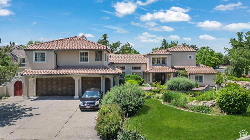 Mediterranean / spanish-style house featuring a garage, concrete driveway, a tiled roof, stucco siding, and a front lawn